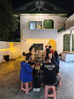 A group of people seated around a table outdoors at night, with a building in the background. - Handora Cultural and Creative Hotel (Vientiane)