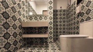 Une salle de bain avec un carrelage décoratif, des toilettes, un lavabo et un miroir.