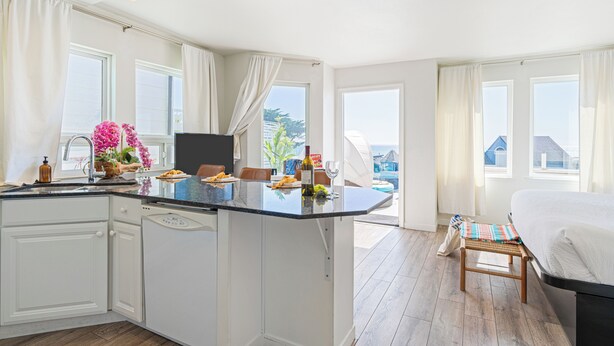 Et moderne køkken med en central ø, lyse skabe og et spiseområde med bænk.