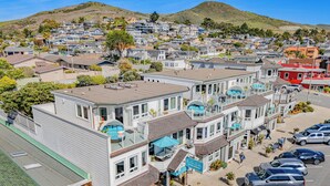 Un edificio residencial de varios pisos con balcones, una calle en primer plano y un paisaje montañoso al fondo.