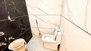 Ein Badezimmer mit Toilette, Eimer und Duschschlauch.