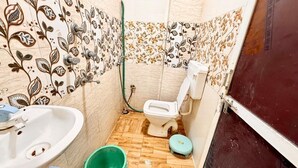 Ein kleines Badezimmer mit Toilette, Waschbecken und einem grünen Eimer.