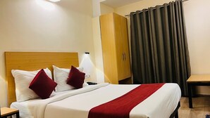 Un lit bien fait, avec une literie blanche et rouge, une tête de lit en bois, une table de chevet avec une lampe et une armoire fermée par un rideau.