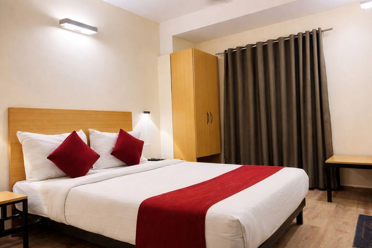 Una habitación de hotel con cama, mesita de noche, armario y cortina.