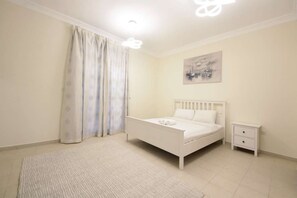 A bedroom with a bed, a nightstand, a painting, and a window with curtains. - 5BR Villa With Private Swimming Pool (Dubai)