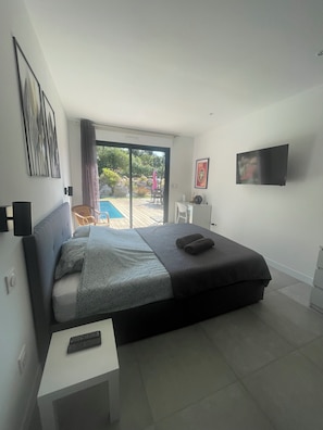 A modern bedroom with a bed, a TV, a small table, and a view of the outdoors.