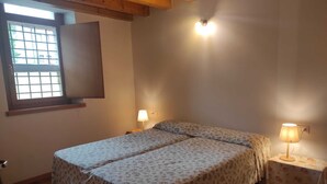 Ein Schlafzimmer mit zwei Betten, Holzdielenboden, einem Fenster mit Blick und zwei Nachttischlampen.