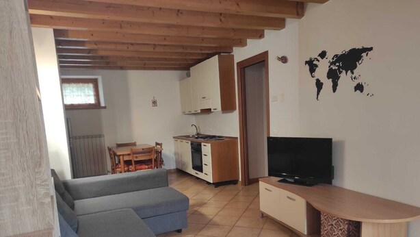 Ein gemütlicher Wohnraum mit einer Couch, einem Fernseher, einer Küchenzeile und einer Weltkarte an der Wand.