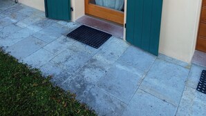 Entrada de un edificio con una puerta de madera y otra verde, un ventanal pequeño y una lámpara en la pared.