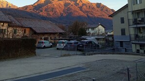 Ein Parkplatz mit Autos, ein Gebäude mit Balkon und ein Berg im Hintergrund.