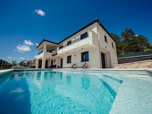 Ein modernes, zweistöckiges Haus mit Schwimmbecken im Vordergrund.