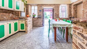 Una cocina rústica con paredes de ladrillo visto, un comedor con mesa y sillas, y vistas al exterior a través de una puerta.