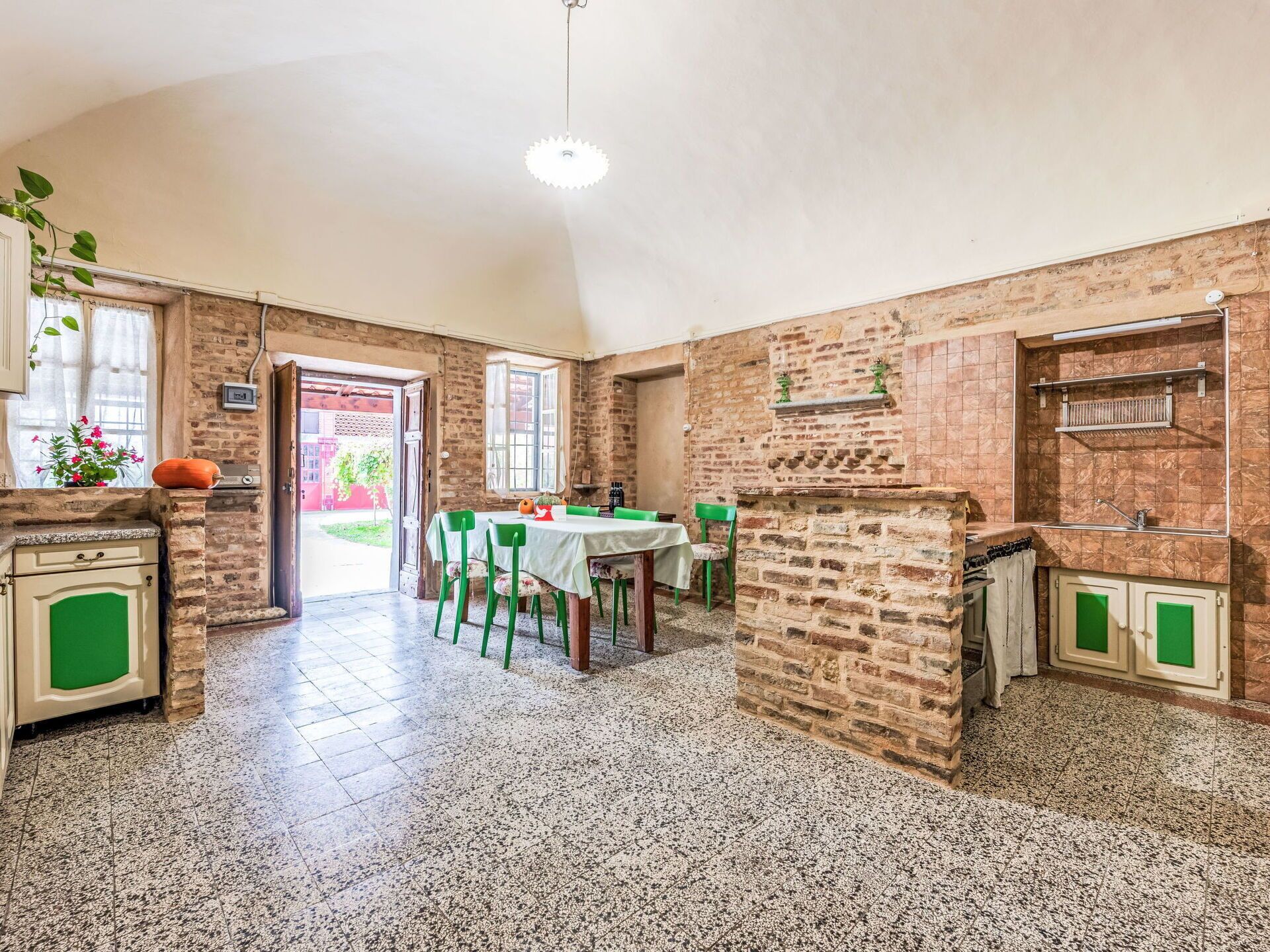 A spacious kitchen with a dining area, featuring exposed brick walls, granite countertops, and a tiled floor.