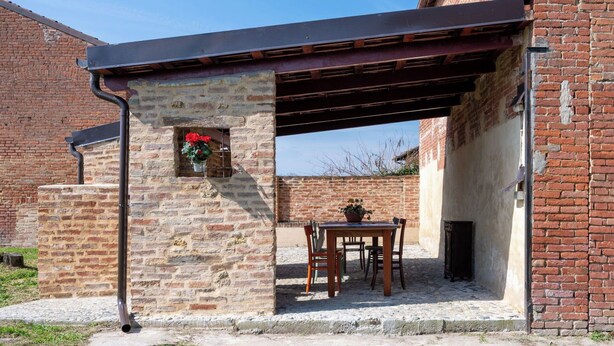 Un edificio de piedra con un patio cubierto, un muro de ladrillo y una pequeña mesa con sillas.