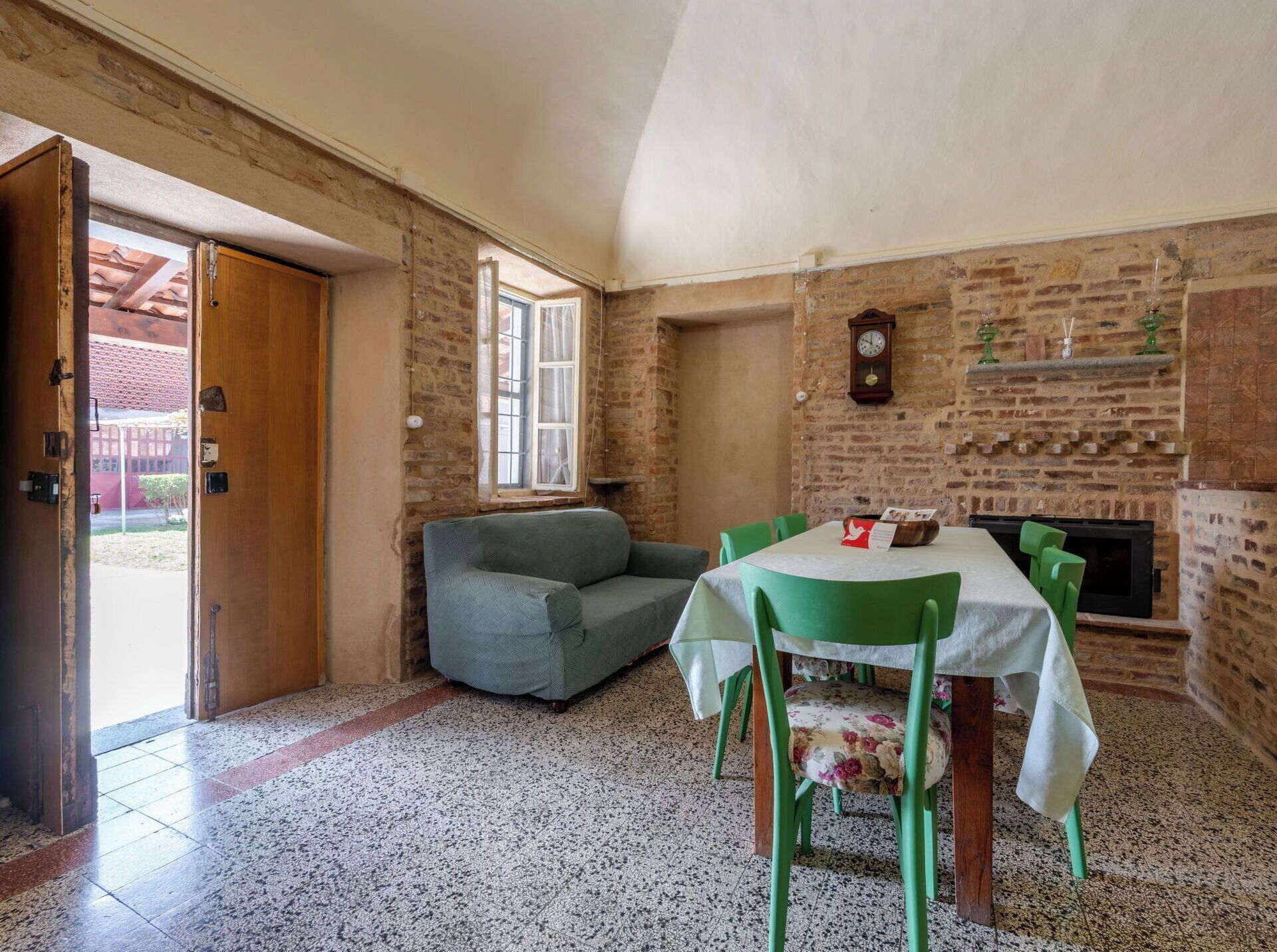 A room with a dining table, chairs, a sofa, a fireplace, and a clock on the wall.