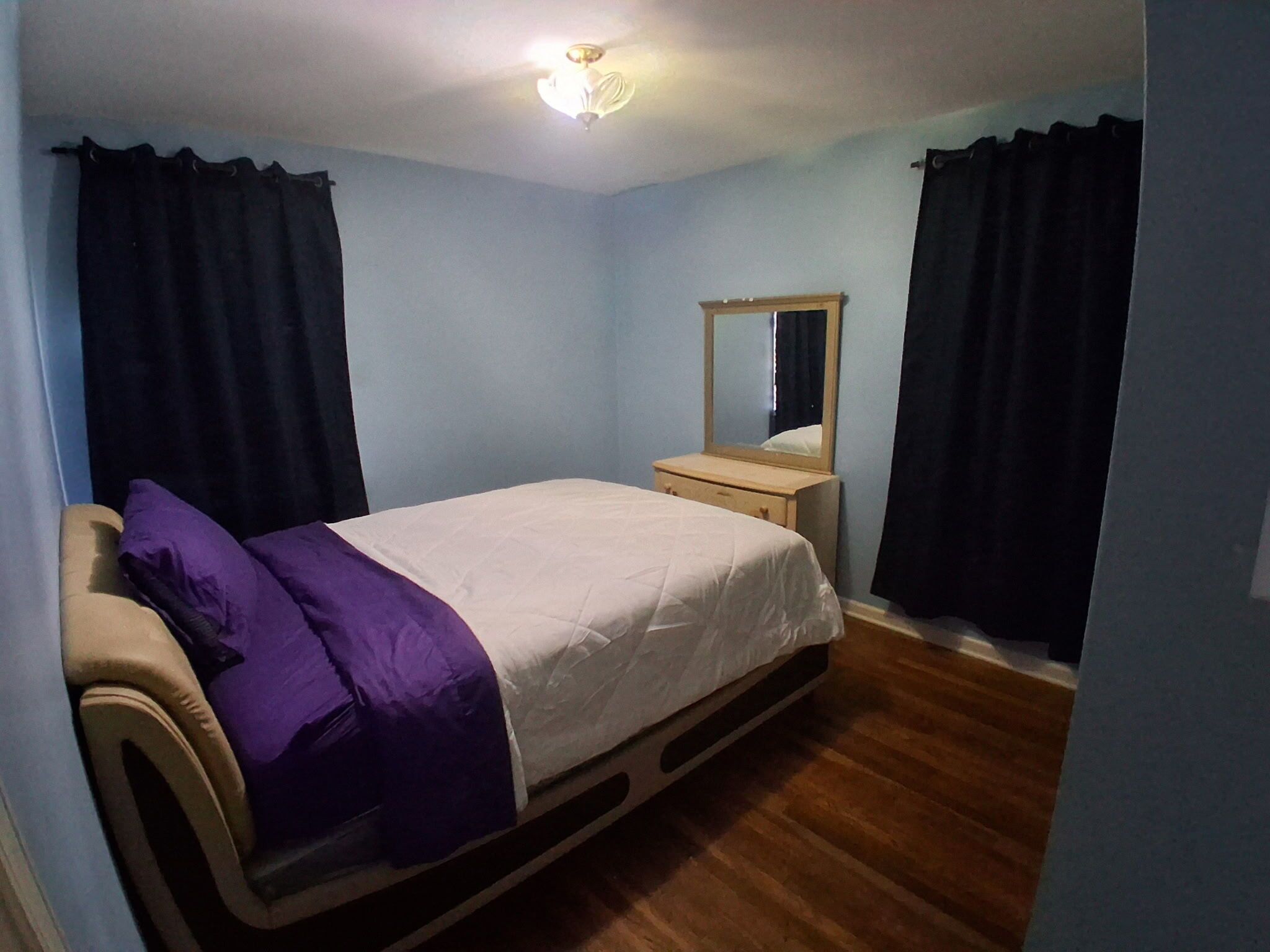 Une chambre à coucher avec un lit, une commode, un miroir et un luminaire au plafond.