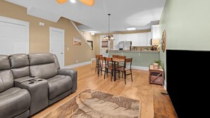 A living room with a gray leather sofa, wooden dining table, and chairs, a ceiling fan, and a kitchen area with white cabinets and a green island. - 3 Bedroom Beach and Golf Getaway (North Myrtle Beach)