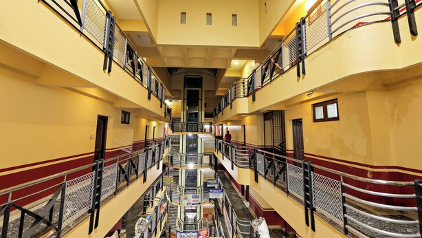 A multi-level atrium with a central staircase, railings, and a variety of signs and banners. - Landmark INN (Kasaragod)