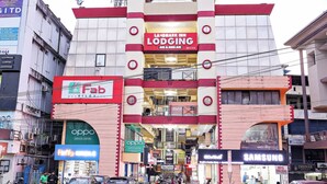 A Landmark Inn Lodging building with a prominent red and white facade, multiple floors, and various commercial establishments on the ground floor. - Landmark INN (Kasaragod)