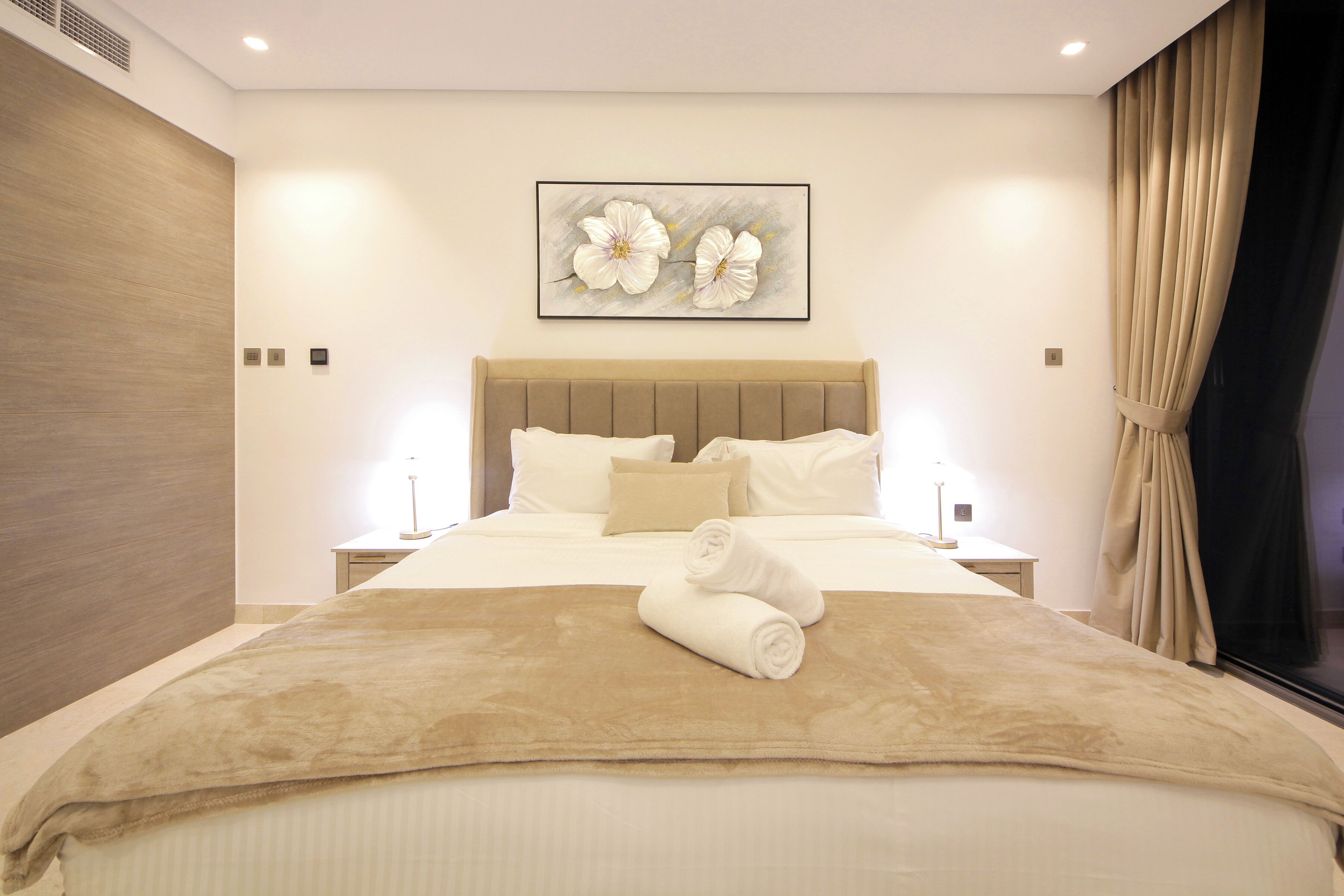 Quarto de hotel moderno com uma cama grande, cabeceira, mesa de cabeceira e uma obra de arte fixada na parede.