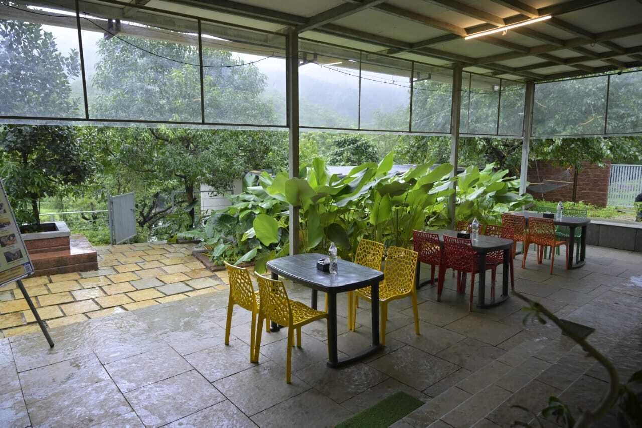 An outdoor patio area with a covered seating area, large windows, and potted plants.