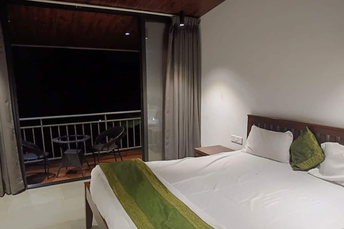 A hotel room with a bed, a small table, a chair, and a balcony with a railing.