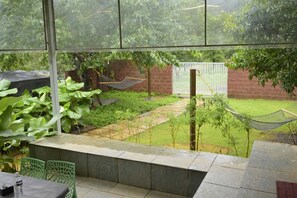A patio area with a table and chairs, a hammock, and a view of a garden with a brick wall and a white fence. - The Meadows Resorts (Paud)