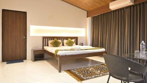A modern hotel room with a wooden ceiling, a bed with green and white bedding, a bedside table, a glass table with chairs, a large window with curtains, and an air conditioning unit. - The Meadows Resorts (Paud)