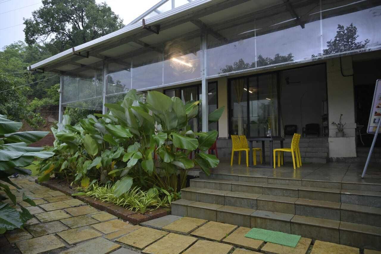 A building with a covered entrance, large windows, and a small outdoor seating area with yellow chairs.