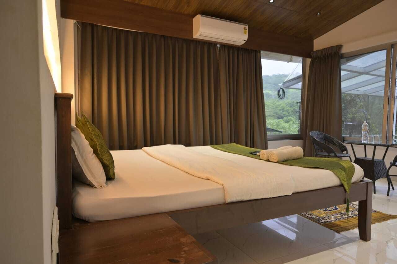A single bed with a wooden headboard, a small table with chairs, and a view of greenery outside.