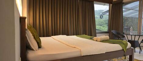A single bed with a wooden headboard, a small table with chairs, and a view of greenery outside.