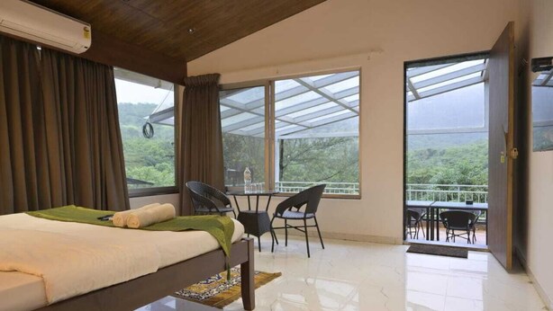 A bedroom with a bed, a table, chairs, and a balcony with a view of greenery. - The Meadows Resorts (Paud)