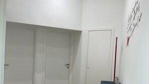 Ett rum med trägolv, en vit dörr, en vit vägg med en röd och svart skylt samt ett litet bord med en tallrik och en flaska.