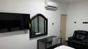 A hotel room with a bed, a desk with a chair, a black leather chair, a TV mounted on the wall, and an air conditioning unit. - Zab's Suite Hotel  (Accra)