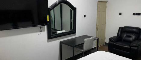 Habitación de hotel con cama, escritorio con silla, sillón de cuero negro, televisor montado en la pared y unidad de aire acondicionado.
