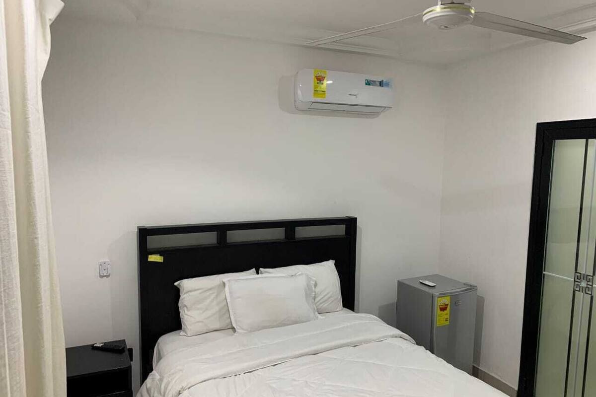 A hotel room with a bed, a nightstand, a small desk, an air conditioning unit, and a wardrobe.