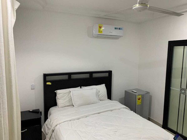 A hotel room with a bed, a nightstand, a small desk, an air conditioning unit, and a wardrobe.