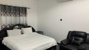 A bedroom with a bed, a chair, a nightstand, and a wall-mounted air conditioner. - Zab's Suite Hotel  (Accra)