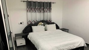 A bedroom with a bed, two bedside tables, a nightstand, a drawer, and a curtain with a plaid pattern. - Zab's Suite Hotel  (Accra)
