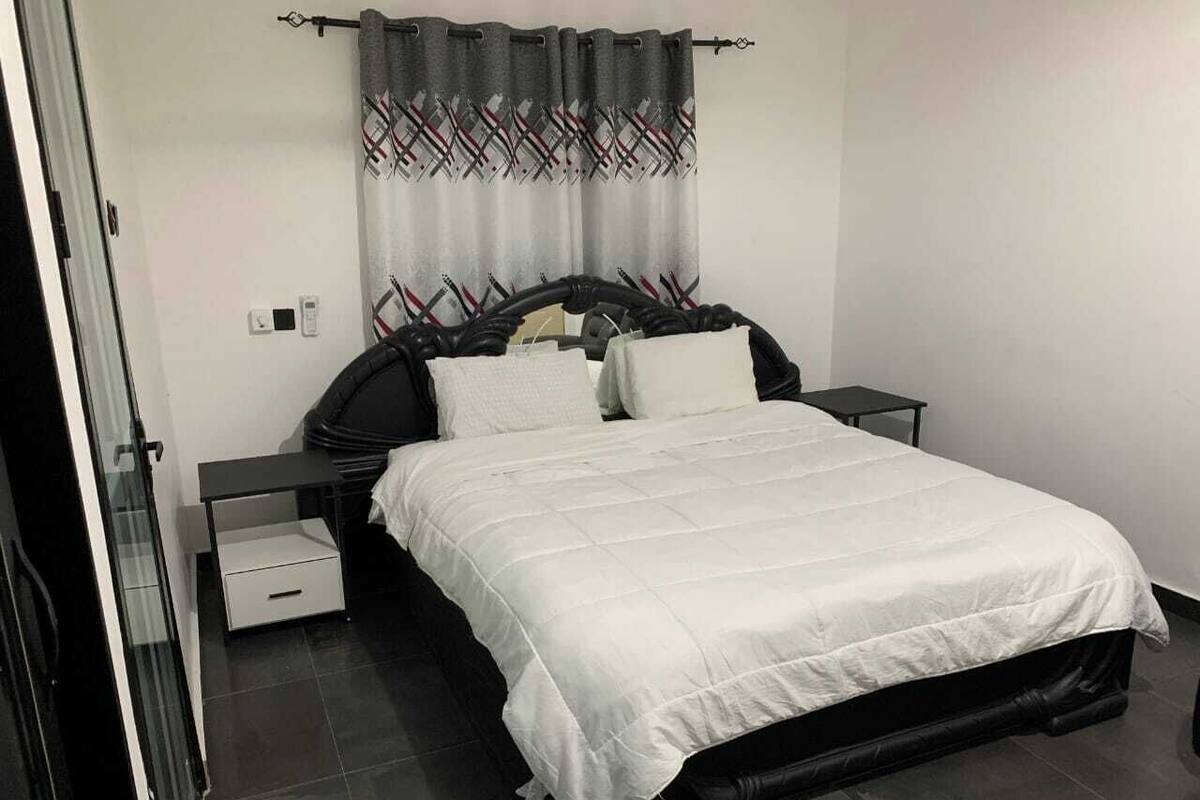 A bedroom with a bed, two bedside tables, a nightstand, a drawer, and a curtain with a plaid pattern.