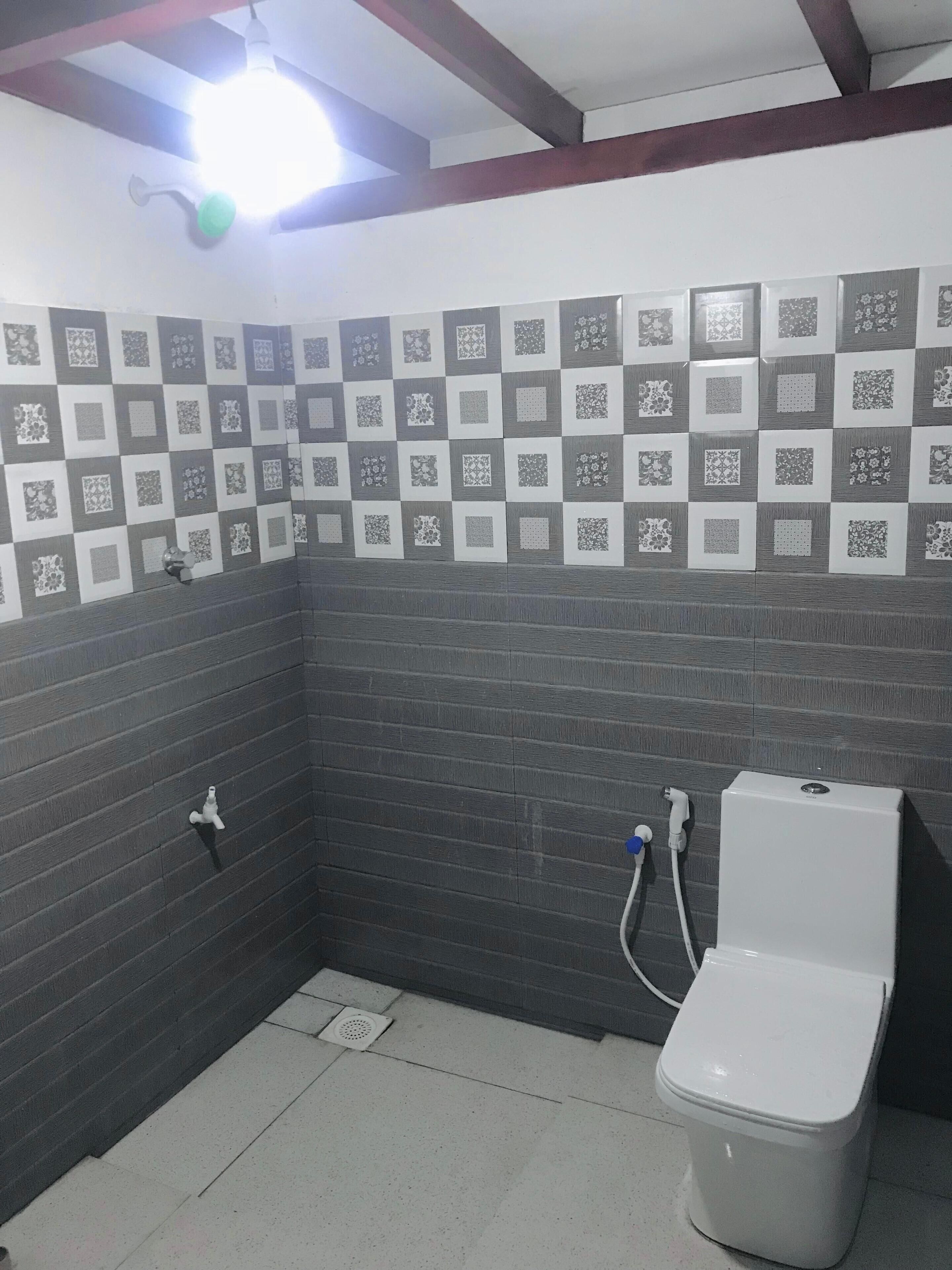 Un baño pequeño con inodoro, lavamanos y ducha. Las paredes están cubiertas de azulejos con un diseño de cuadros.