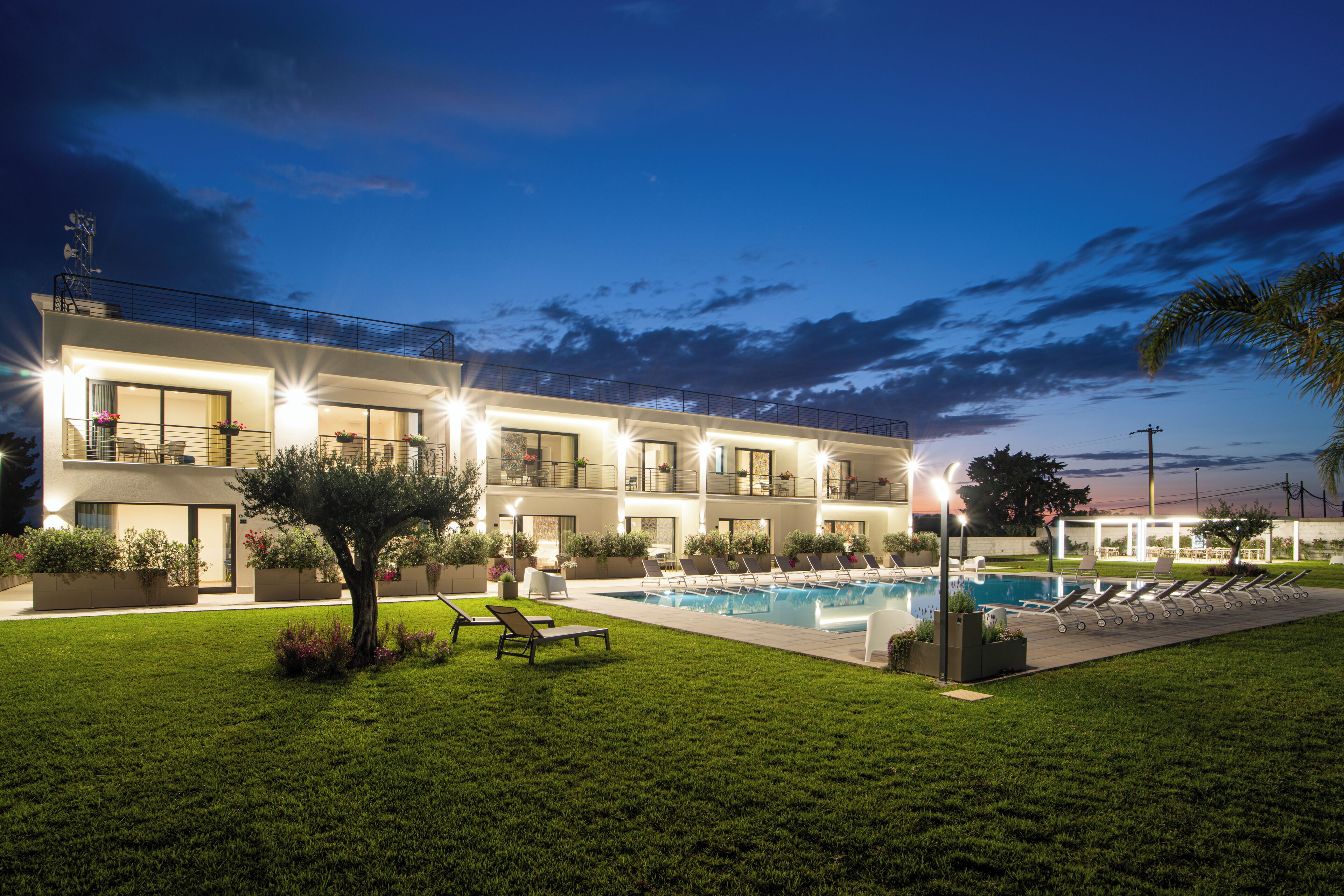 Un hotel moderno con piscina, varios balcones y césped bien cuidado.