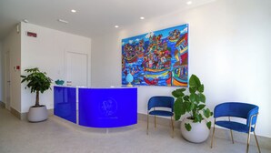Un espace d’accueil avec un comptoir bleu, deux chaises bleues, un grand tableau coloré et des plantes en pot.