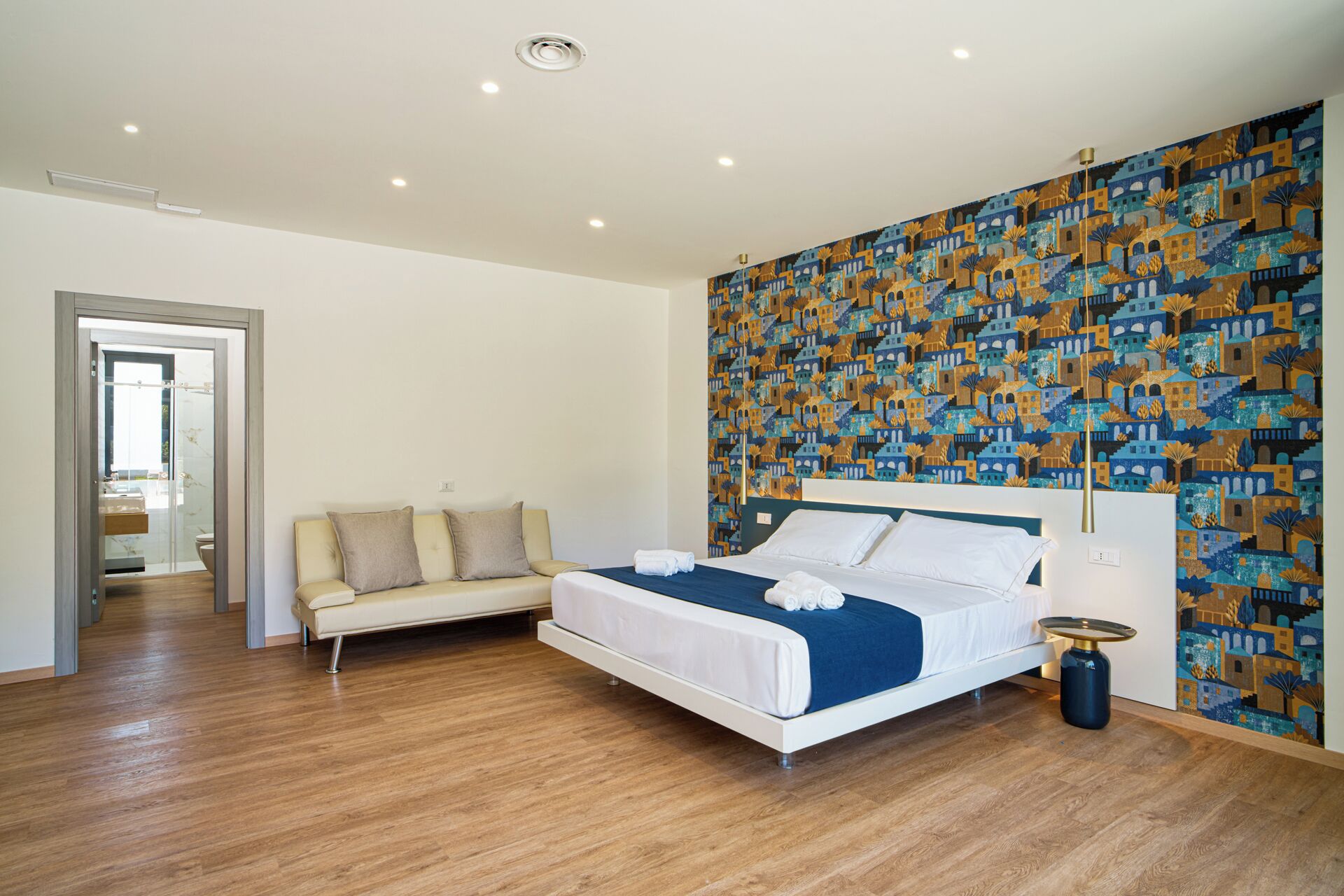 A modern bedroom with a bed, a sofa, and a patterned wall.