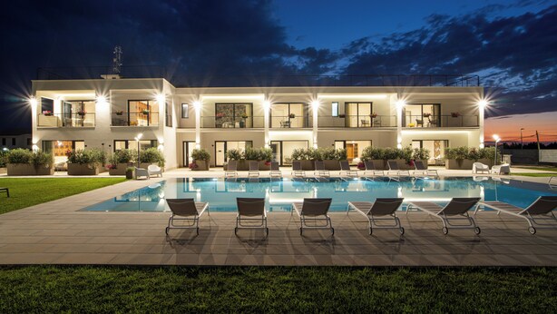 Un bâtiment moderne à deux étages, doté d’une piscine, de chaises longues et de plantes en pot.