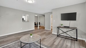 A modern living room with a round table, a TV on a stand, and a hallway leading to a dining area. - Comfy stay with patio and laundry near Atlanta (Stockbridge)