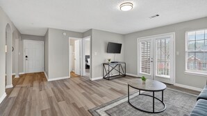 A spacious living room with hardwood flooring, a round coffee table, a flat-screen TV, and a large window with blinds. - Comfy stay with patio and laundry near Atlanta (Stockbridge)