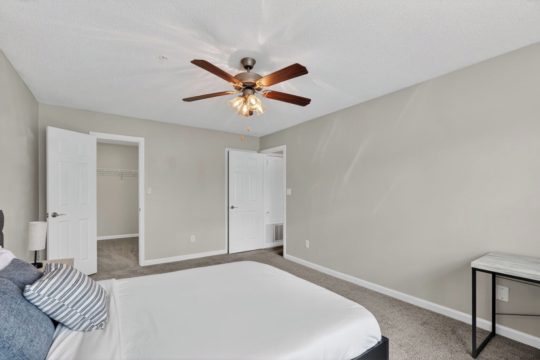 A bedroom with a bed, a ceiling fan, a desk, and two doors.
