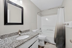 Een badkamer met een witte wastafel, een spiegel, een toilet en een douche met gordijn.