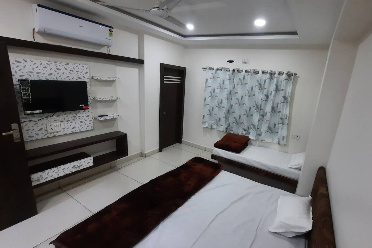 A modern bedroom with a bed, a TV mounted on the wall, a built-in shelf, and a window with curtains.